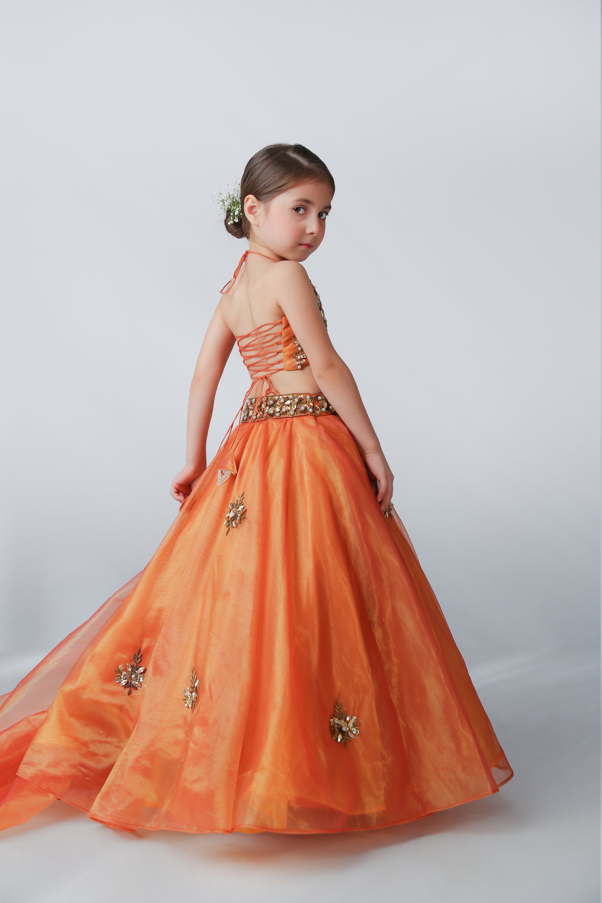 Young girl in an orange formal gown with floral embellishments on a white background